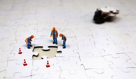 Um grupo de pessoas em miniatura se reúne em torno de uma peça perdida em um quebra-cabeça