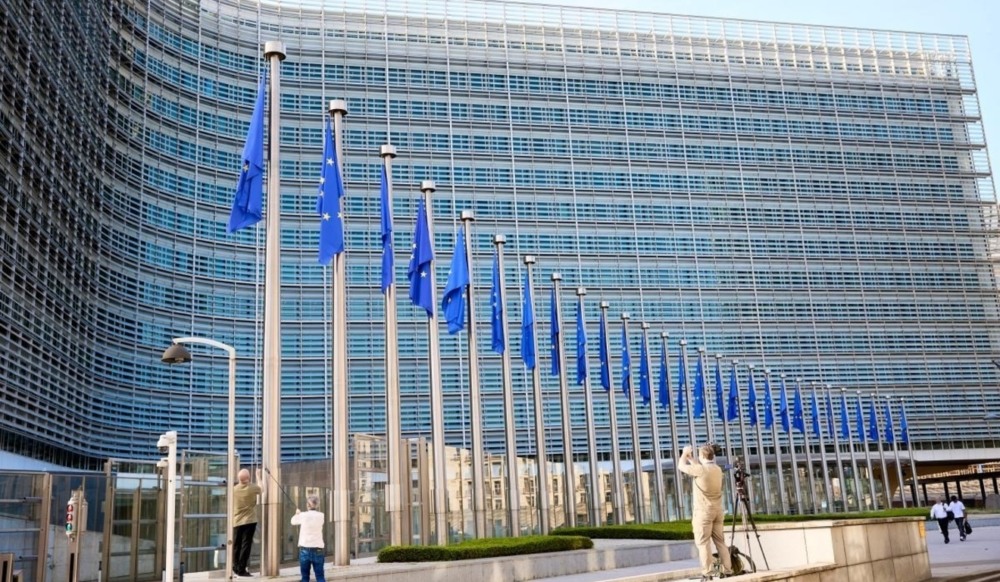 Edifício Berlaymont, sede da Comissão Europeia em Bruxelas, com uma fileira de mastros e bandeiras da União Europeia hasteadas Edifício Berlaymont, sede da Comissão Europeia em Bruxelas, com uma fileira de mastros e bandeiras da União Europeia hasteadas