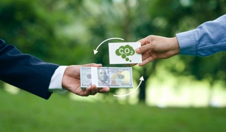 Duas pessoas trocam dinheiro por um cartão com símbolo de CO2, representando o mercado de créditos de carbono Duas pessoas trocam dinheiro por um cartão com símbolo de CO2, representando o mercado de créditos de carbono