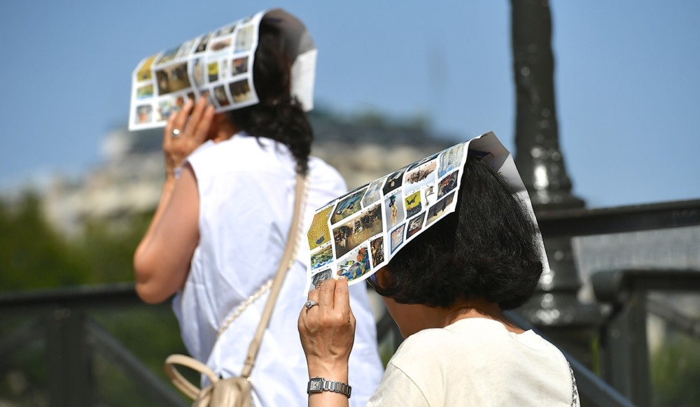 Duas mulheres usando folhetos turísticos coloridos como proteção improvisada contra o sol forte em um dia de verão europeu