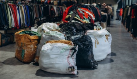 Vários sacos de roupas no meio de uma loja com araras de roupas ao fundo