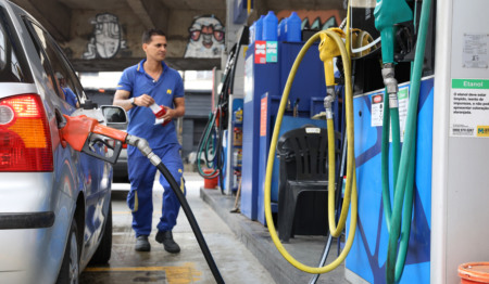 Foto de um carro parado ao lado de bombas de um posto de gasolina, com um frentista ao fundo Foto de um carro parado ao lado de bombas de um posto de gasolina, com um frentista ao fundo