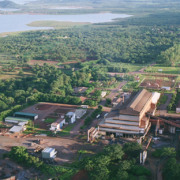Foto de uma planta industrial rodeada por verde, com um rio ou lago ao fundo