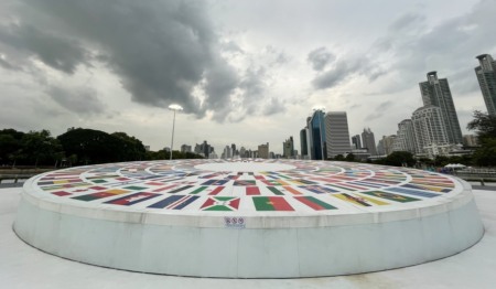 Monumento circular em praça com imagens de bandeiras de vários países. Ao fundo estão prédios, e o véu está carregado de nuvens Monumento circular em praça com imagens de bandeiras de vários países. Ao fundo estão prédios, e o véu está carregado de nuvens