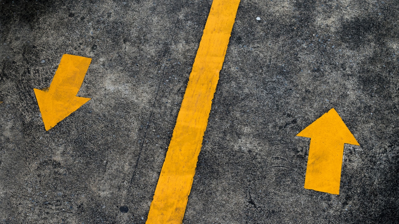 Via pavimentada com duas setas pintadas em amarelo em direções opostas